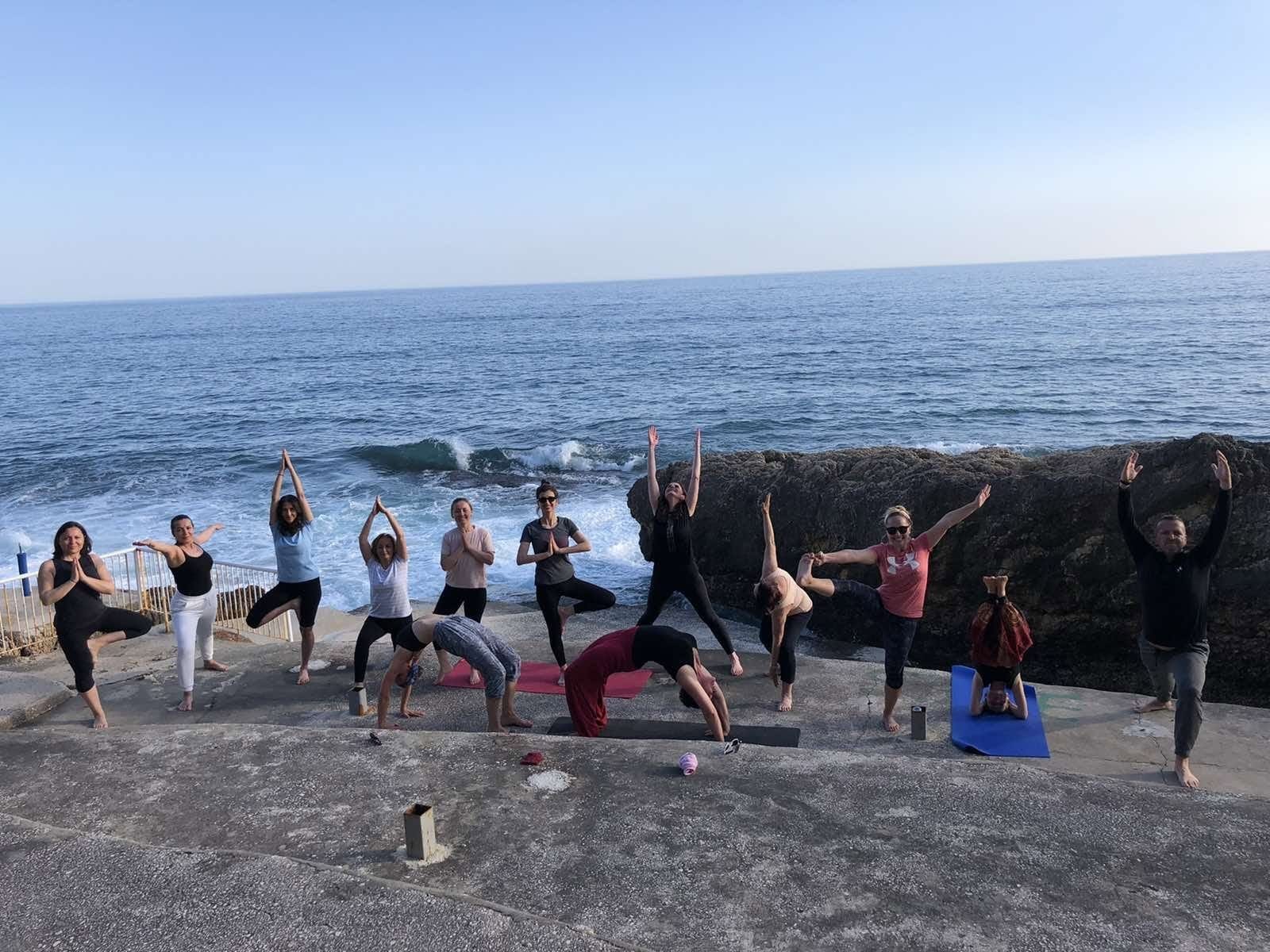 Një grup duke praktikuar poza yoga-je mbi shkëmbinj pranë detit